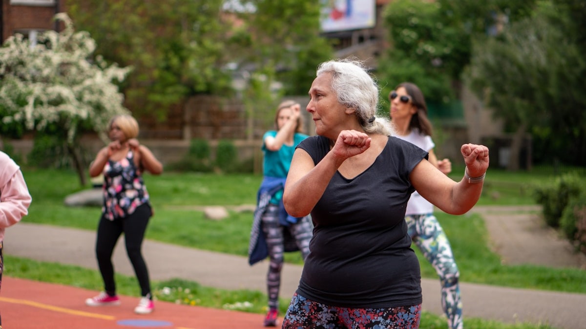 An older woman does exercises at an outdoor fitness class.